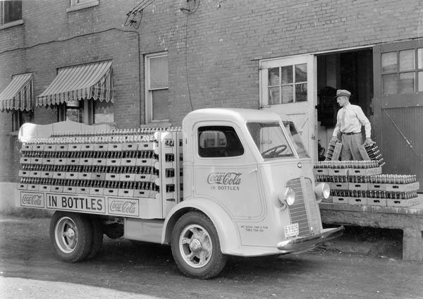 Delivery man loading bottle cases of Coca-Cola soda onto the open bed of an International C-300 delivery truck, 1936